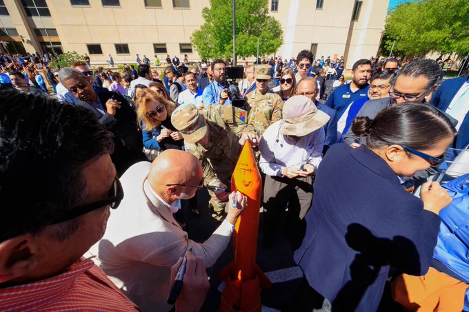 A crowd gathers around to sign a ceremonial orange rocket at the grand opening of UTEP's Advanced Manufacturing and Aerospace Center.