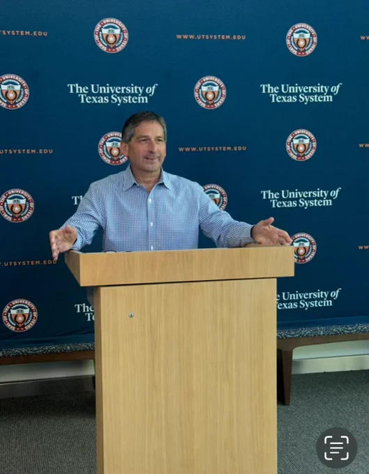 Board of Regents Chairman Kevin Eltife stands behind a podium with a UT System backdrop behind him. 