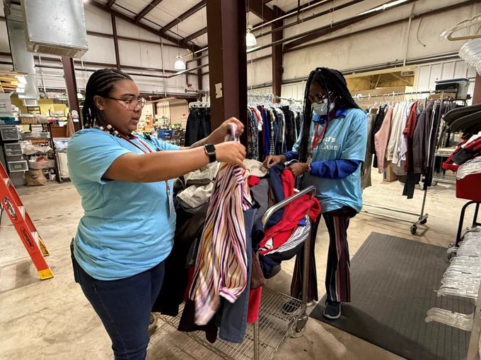 Two staff members are hanging up clothes.