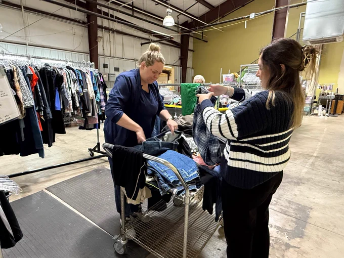 Two staff members are looking through clothes to hang.