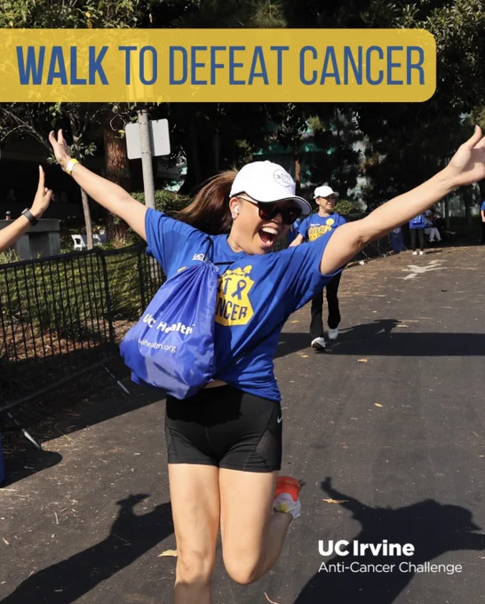 Participant with arms raised in celebration at the 'Walk to Defeat Cancer' event, wearing a blue 'Defeat Cancer' shirt and a UC Irvine Anti-Cancer Challenge cap.