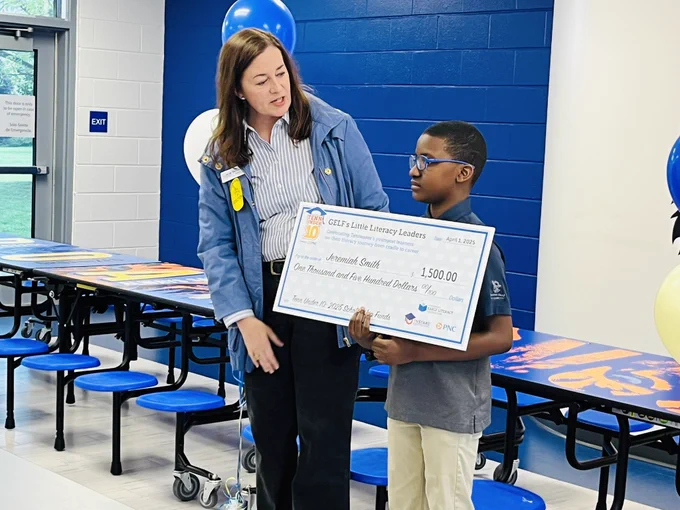 Boy holding a big check standing next to a lady talking about the check