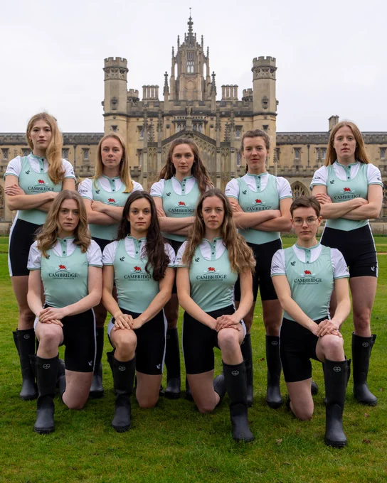 The Cambridge University Lightweight Women's Crew in white and Cambridge Blue and black wellies in front of the iconic spires of St John's College. They are arranged in two rows - five in the back with the cox, standing, and four kneeling on one knee in the front.
