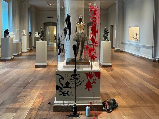 Washable black paint to representing oil and red paint to represent blood is seen smeared on the protective cover of Edgar Degas’ Little Ballerina statue by climate protesters. 
Photo credit : Declare Emergency