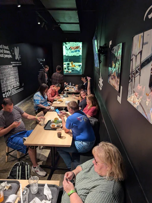 A group of people sitting at tables in a restaurant. One woman is waving at the camera.