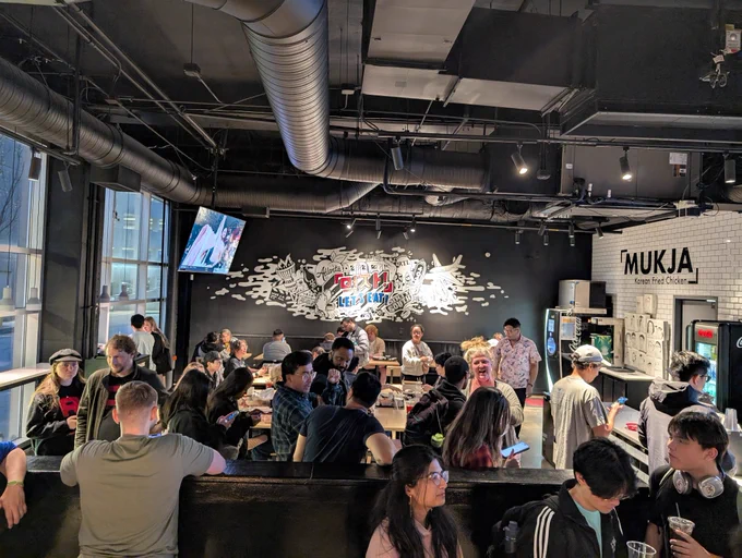 Large groups of people standing and sitting at tables in a restaurant.