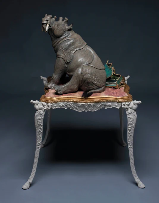 sculpture of a rhinoceros looking creature with long saber teeth sitting on a fancy table