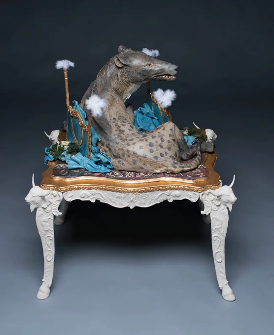 sculpture of a spotted jackal like creature on a fancy bed positioned on a fancy table