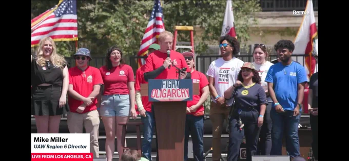 Mike Miller speaking on a stage with a row of UAW members standing behind him