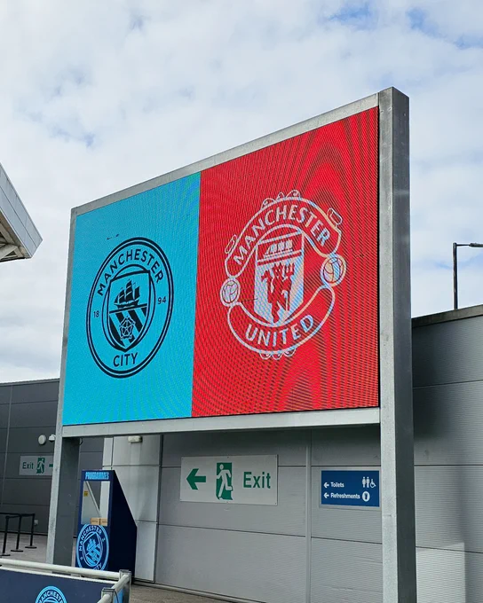 A sign at the Joie Stadium depicting the Man City and United crests next to each other.