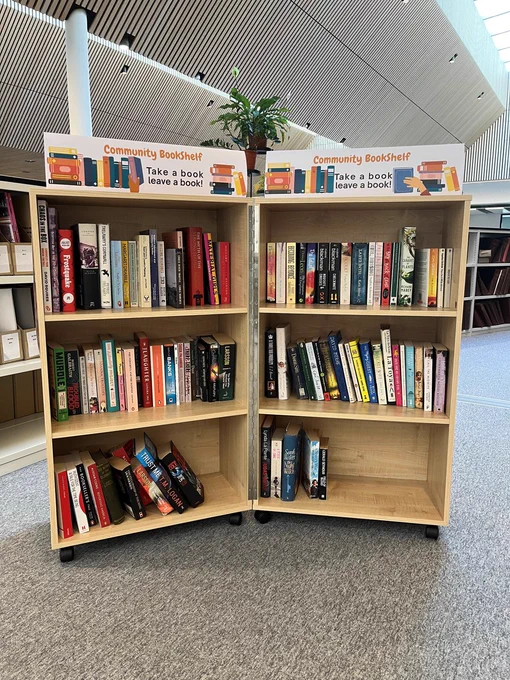 Front facing picture of the Community Bookshelf. Double bookcase with three shelves on wheels with a selection of books on the shelves. 