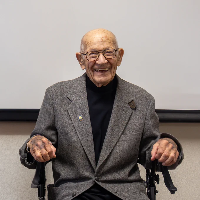 A man sits down and smiles brightly.