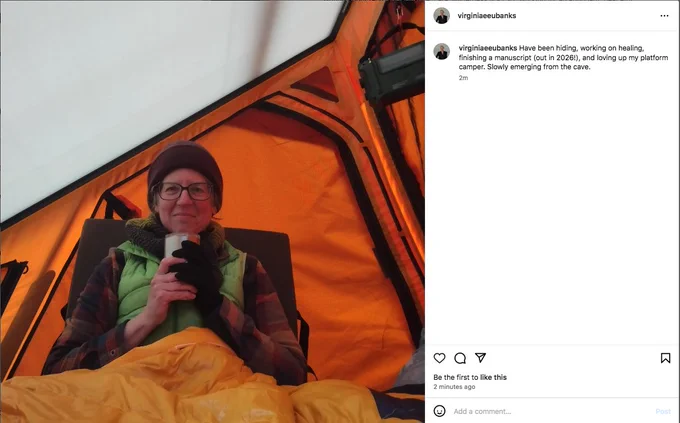 An Instagram post featuring a middle aged white man sipping tea in a bright orange tent and smiling at the camera, which reads "Have been hiding, working on healing, finishing a manuscript (out in 2026!), and loving up my platform camper. Slowly emerging from the cave." 