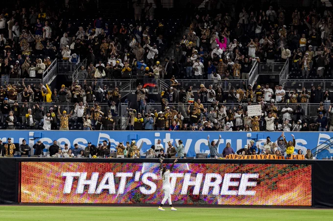 Fernando Tatis Jr. holding his hands up toward the fans in right field after the third out of the 9th inning at Petco Park. The LED board on the right field wall reads "That's Three."