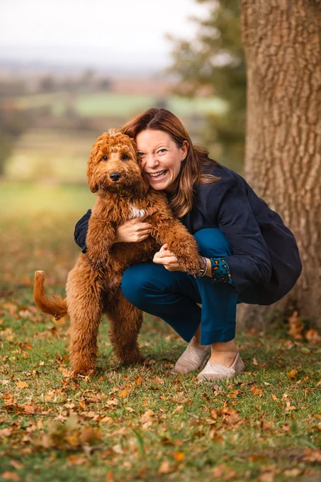 A woman smiling and crouching down holding her dog who is stood on two legs