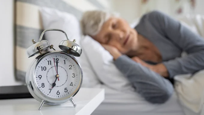 An alarm clock with a long-term care resident sleeping in the background