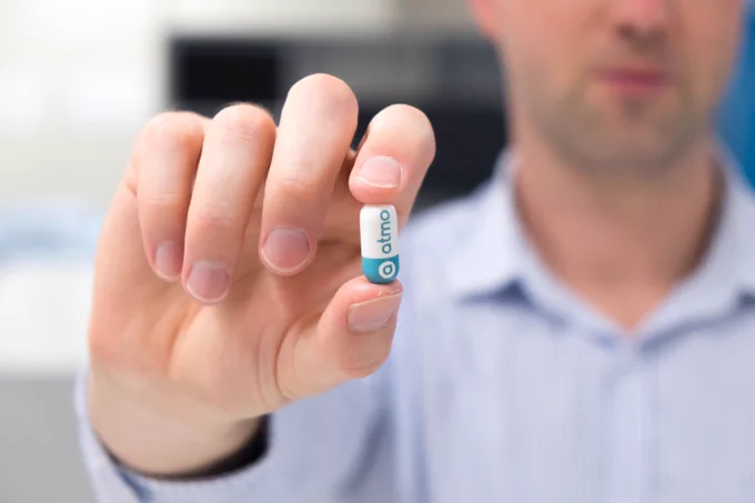 A person holding a pill with the Atmo Biosciences logo on it.