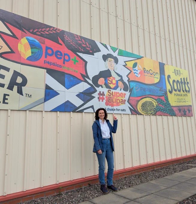 Wendy in front of a banner that says 'Super Cupar' with the Quaker Oats logo above and the Scottish flag to the side.
