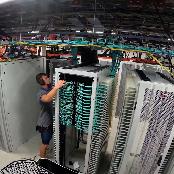 Person working on a server rack in a data center, handling cables.