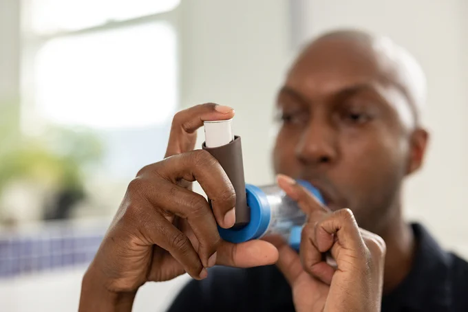 Man holding a brown preventer inhaler with a blue spacer.