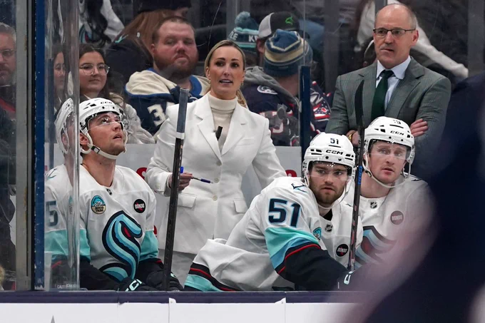 A photo of Jess Campbell behind the bench while Shane Wright sits in front of her.