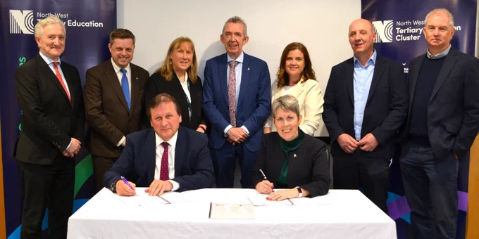 Members of North West Regional College and ATU standing Infront of a North West Tertiary Education blue and white pull up banner whilst two members are seated at a table signing an agreement