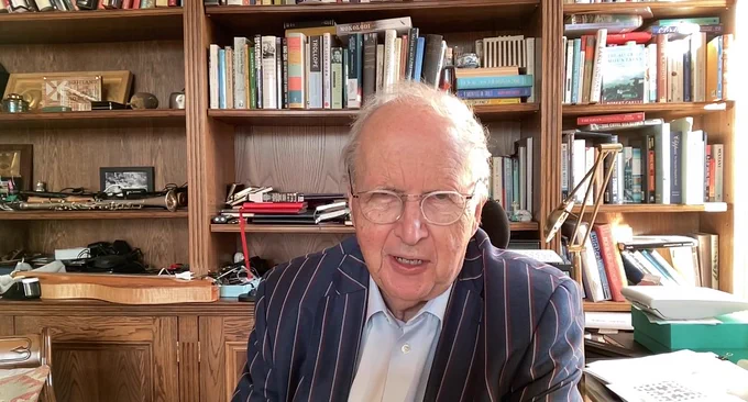 A man sitting in front of bookshelves wearing a striped jacket.