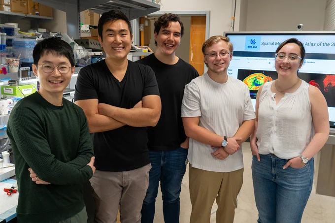 Neuroscientists (from left) Xin Ma, Ramon Sun, Ph.D., Roberto Ribas, Cameron Shedlock and Terry Medina smiling in a lab in front of their brain map, which is publicly accessible to support researchers studying metabolism and the mind. Photo by Jackie Hart.