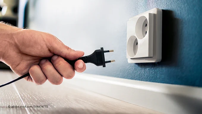 Eine Hand hält einen Stromstecker nahe einer Steckdose.