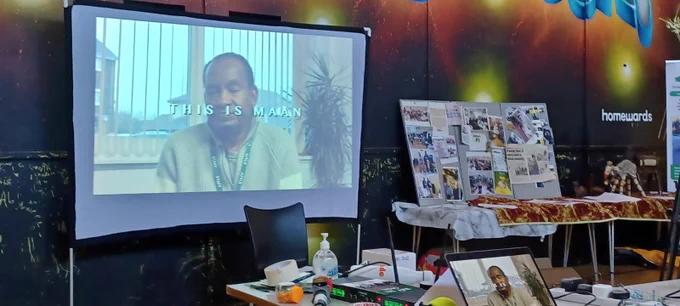 A picture of a projector screen and some stalls at the MAAN 30th anniversary event.