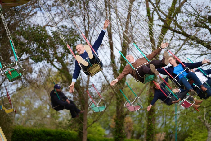 Ed Davey and Ian Roome MP ride on colourful flying swings, arms outstretched and smiling.