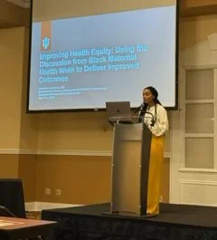 Jasmine Johnson, MD FACOG is at the podium with a PowerPoint presentation in the background. 