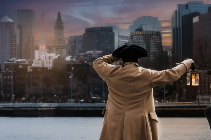 A person in Colonial-era clothing and a tricorn hat stands in front of the modern Boston skyline. 