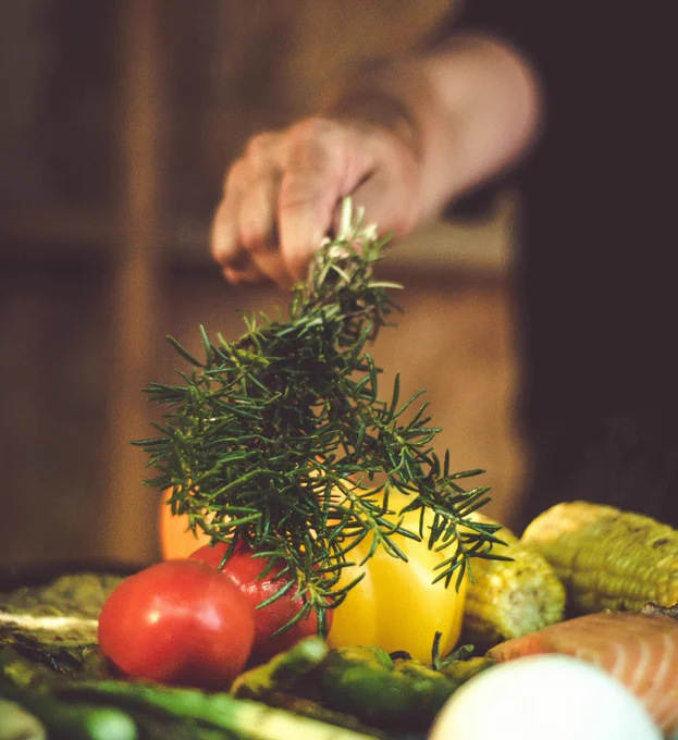 A vibrant assortment of fresh vegetables and herbs, including tomatoes and rosemary, being prepared for grilling.