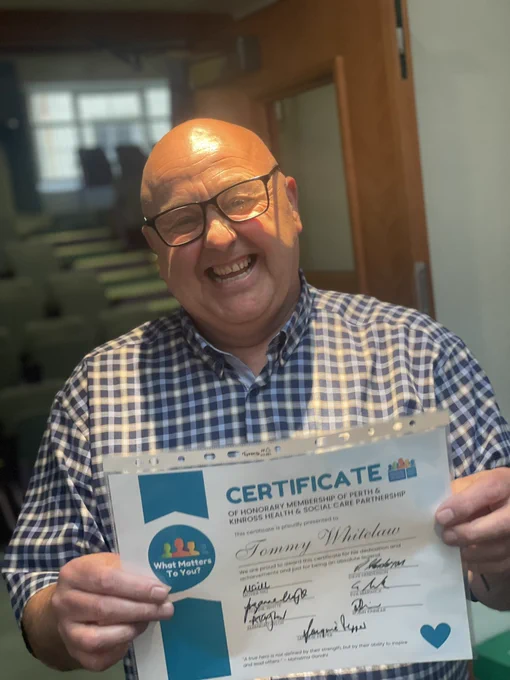 Tommy Whitelaw holding a certificate of honorary membership of Perth and Kinross Health and Social Care Partnership  