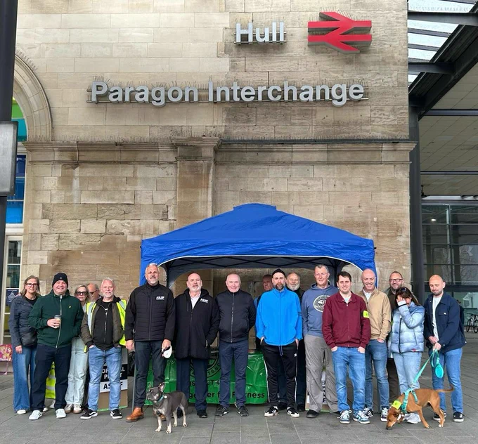 A group of people and dogs standing in a line  in front of Hull train station on an ASLEF picket line
