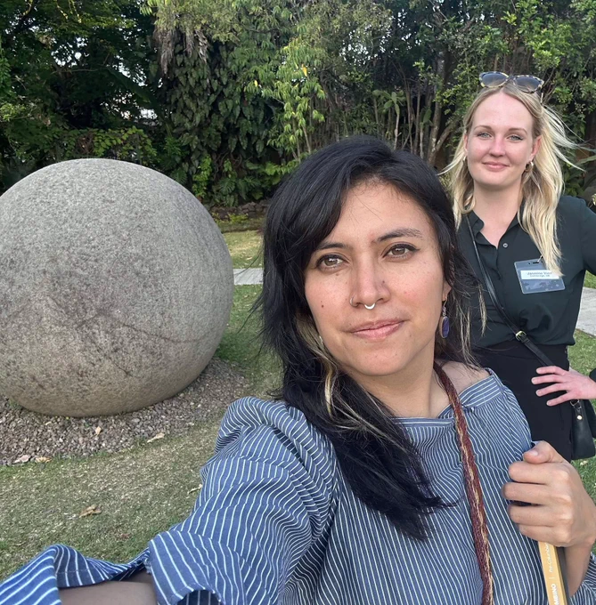 Two women take a selfie with an ancient stone sphere