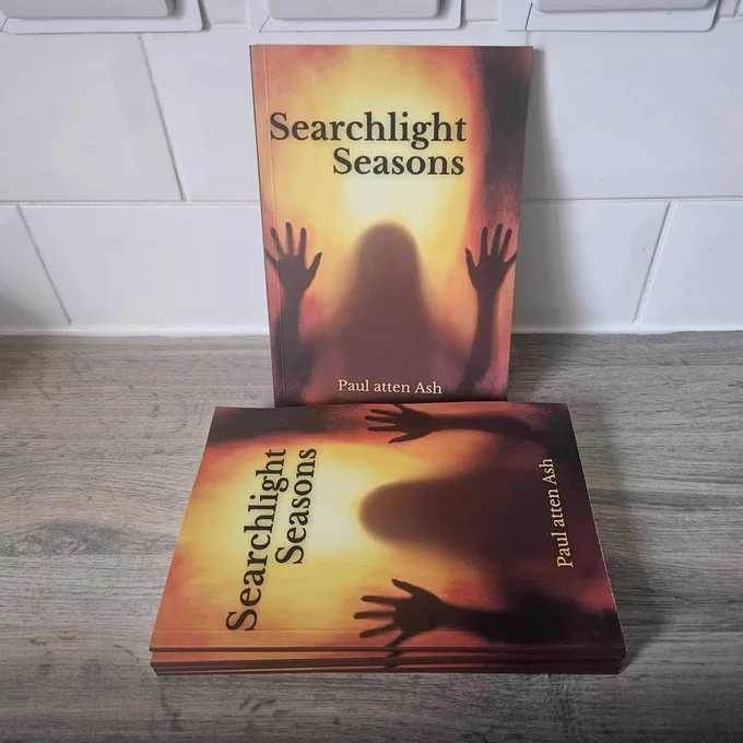 Copies of Searchlight Seasons on a grey counter, propped against a white, tiled wall