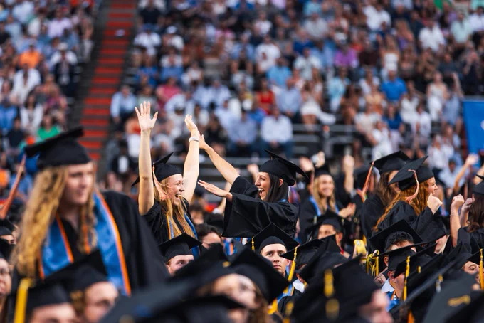 Two graduates cheering in the crowd during the university-wide commencement ceremony