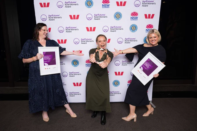 Katelyn Wall (Finalist), Carol Mudford (Winner), and Dimity Smith (Finalist) celebrating with their awards at the NSW Rural Women's Award event, standing in front of a banner with logos.