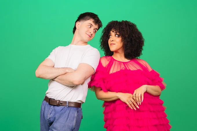 A photo showing two individuals in quirky outfits on a green background 