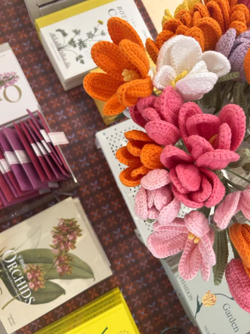 A photo of flower themed books laid down on a patterned table next to some colourful crotched flowers.