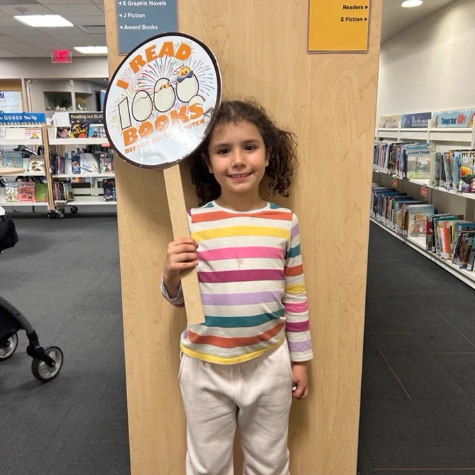 A young girl smiling and holding up a sign that says I read 1000 Books before kindergarten.