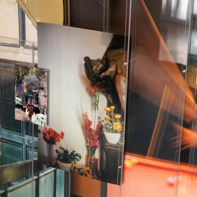 Photographs behind glass – A display of layered photographs behind glass, including an image of a crucifix surrounded by flowers and a protest scene.