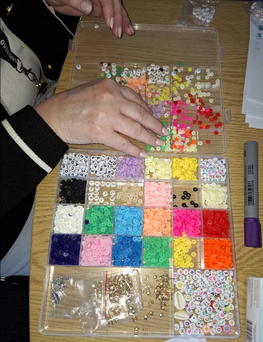 a hand hovering over a colourful collection of beads sorted by colour, shape and theme
