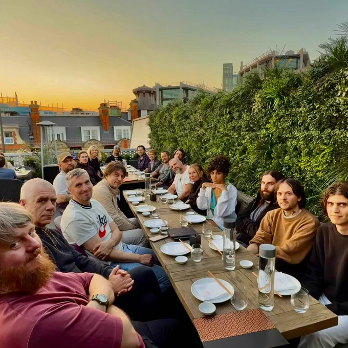 A photo of 19 people surrounding two long dinner tables. Photo taken at CLAP London.