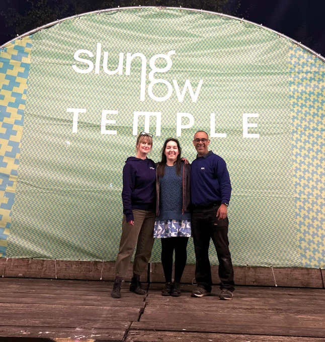 Three smiling members of the Slung Low team standing on the outdoor stage space at Temple