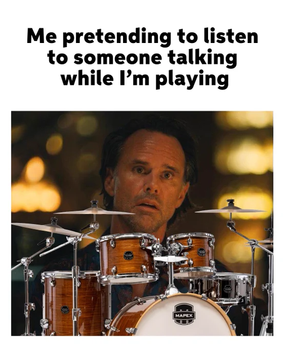 A person sitting behind a drum set with a focused expression, pretending to listen while playing. The text above reads "Me pretending to listen to someone talking while I'm playing.