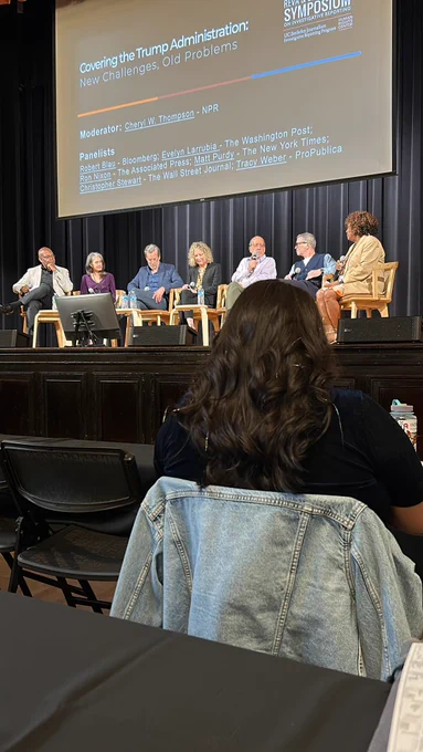 Seven people sitting on a stage, talking