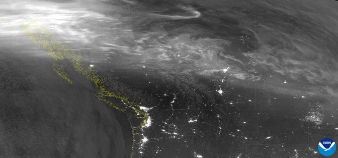 Satellite observation of the northwestern United States and regions farther north, captured in the early morning of May 2, 2025. City lights are visible beneath faint arcs of the aurora borealis across the upper part of the image. The NOAA logo is seen in the lower right corner.